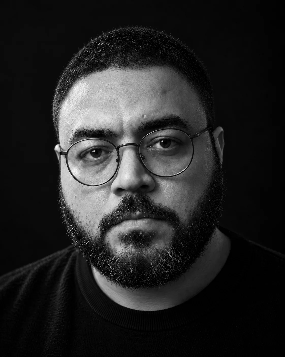 Black-and-white close portrait of Lamek Felix wearing round glasses